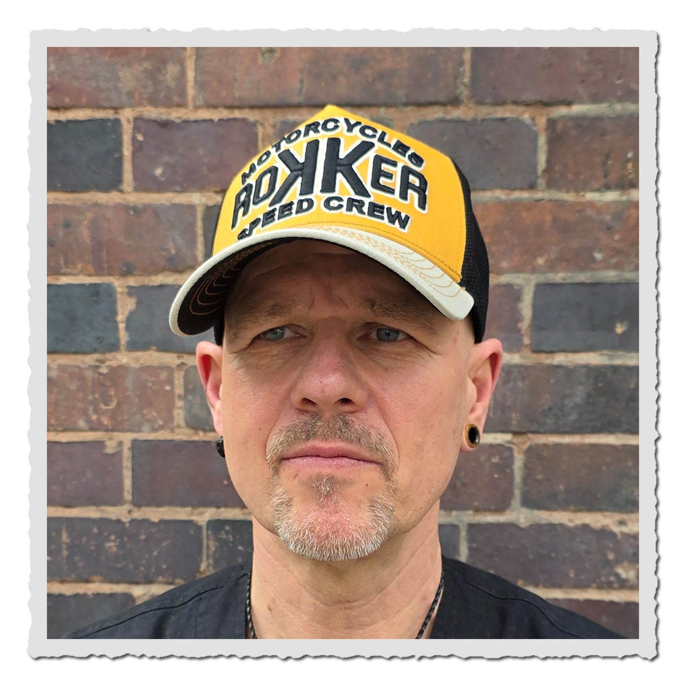 Mann trägt Trucker-Cap in Sand, Creme und Schwarz, schräg von vorne, schwarzes Mesh hinten, weißer Hintergrund.